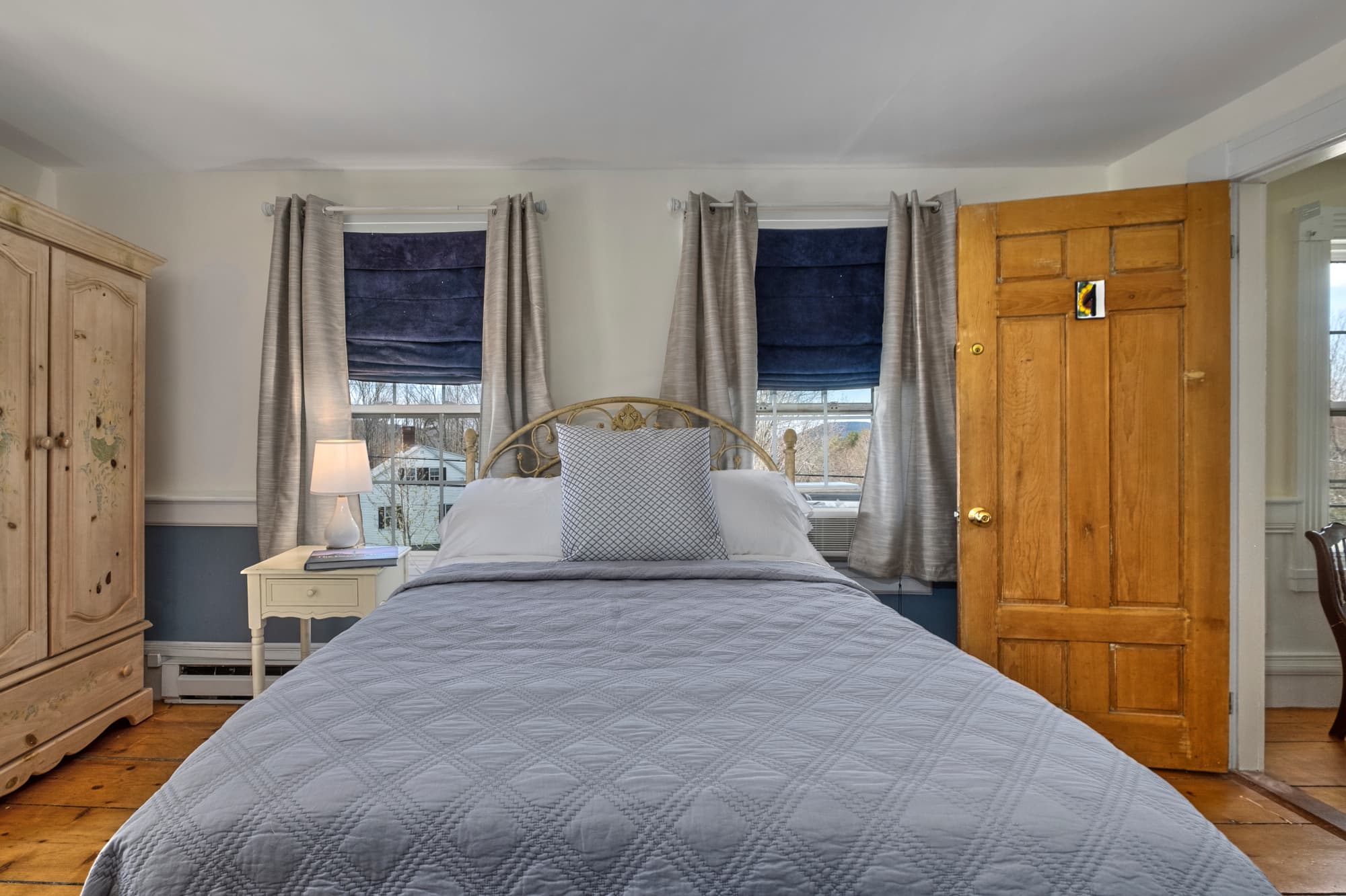 Cozy bedroom featuring a bed with gray bedding, a wooden door, and large windows with blue shades.
